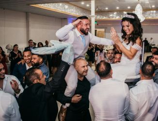 Wedding guests lift a bride on a chair and the groom on their shoulders during a reception dance