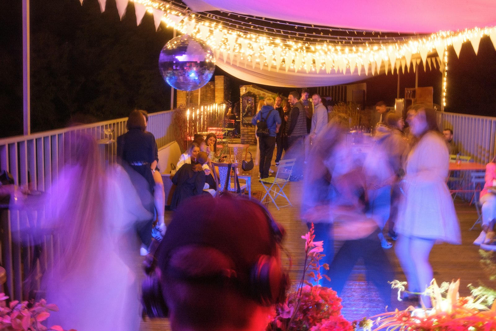 Wedding guests dancing under a disco ball and string lights with pink and purple uplighting
